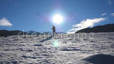 在阳光明媚的日子里，一个面目全非的家伙在雪地草地上用棍子走路。 年轻的徒步旅行者在雪地上跋涉